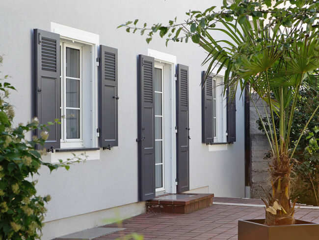 Volets battants en aluminium gris foncé sur une maison moderne en crépi gris clair