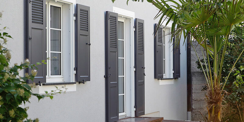 Volets battants en aluminium gris foncé sur une maison moderne en crépi gris clair