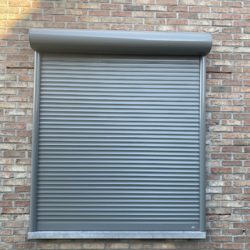 installation de volets roulants avec un caisson arrondi gris sur une façade en brique