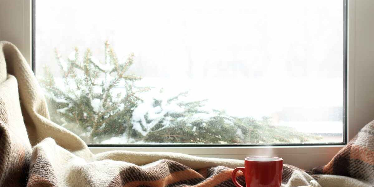 ISOL-isoler-fenetres Fenêtre avec châssis en PVC blanc donnant sur un paysage enneigé et avec un plaid et une tasse rouge devant